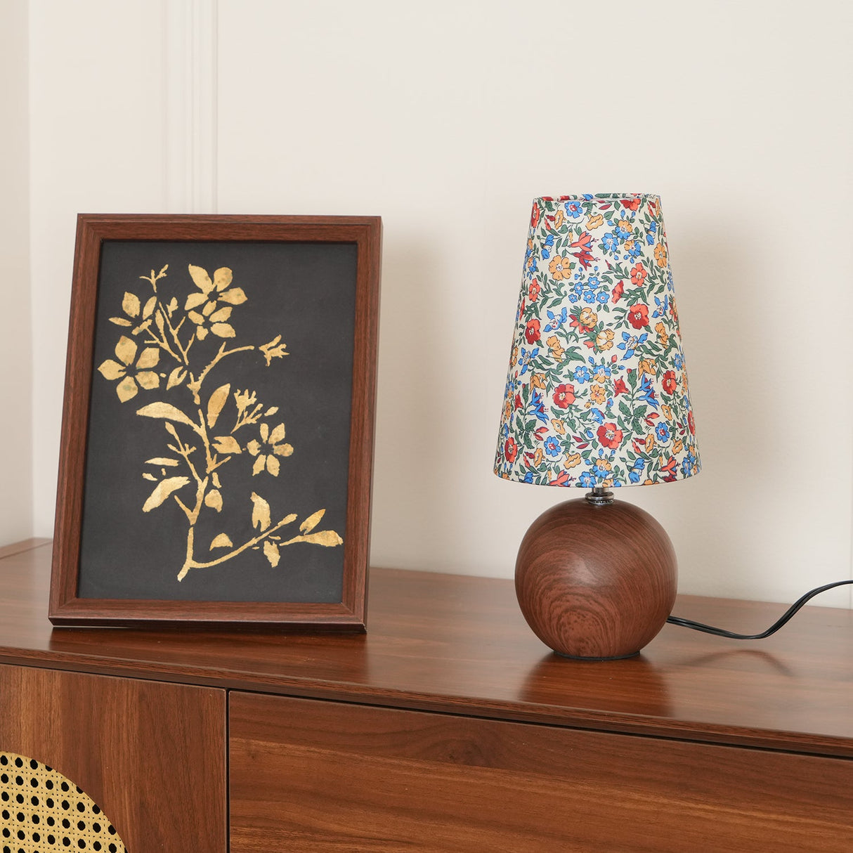 Floral table lamp and framed botanical print on a walnut cabinet