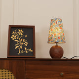 Warm lit floral table lamp on a cabinet beside a dark framed print