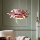 Pink flower pendant light lit against a sage panel wall by an armchair