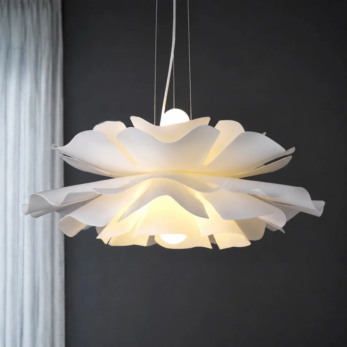 White petal flower pendant light lit against a dark grey wall