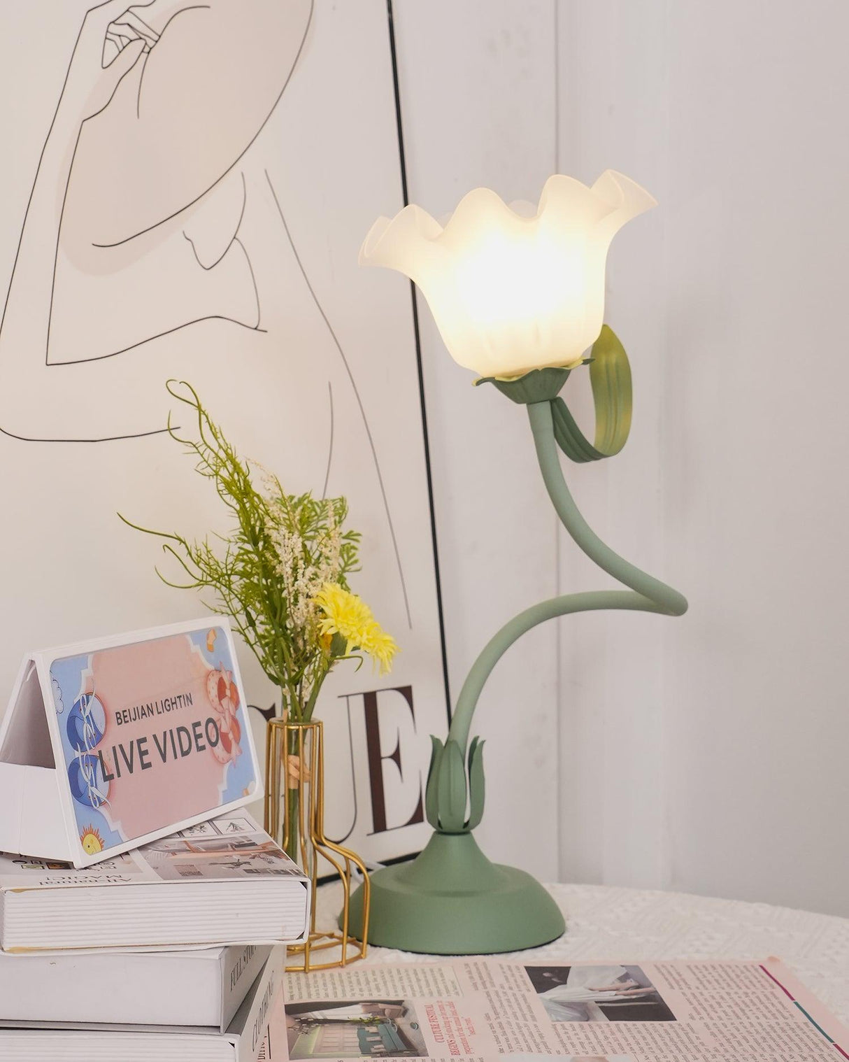 Flower table lamp with a closed bud shade standing beside a slim brass vase