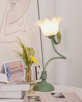 Flower table lamp with a closed bud shade standing beside a slim brass vase