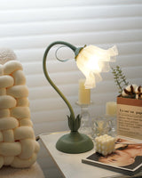 Flower table lamp lit above a candle holder and a stack of open magazines