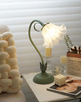 Flower table lamp lit beside pillar candles and a knitted pouf on a side table