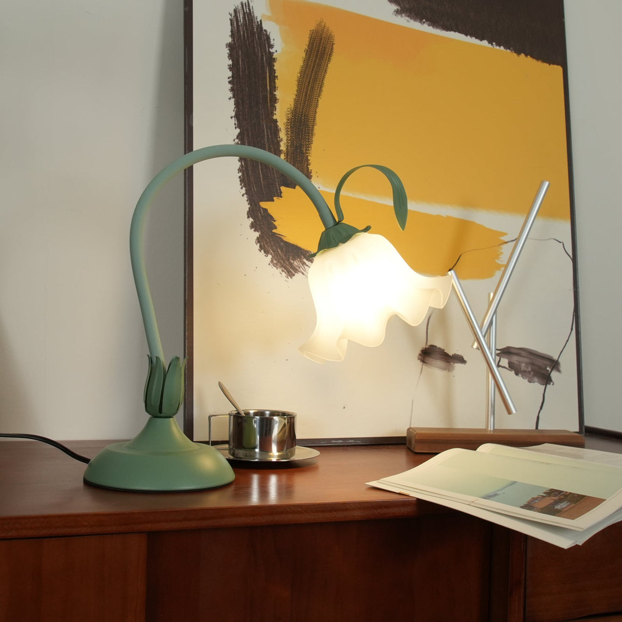 Drooping petal shade lit on the curved stem in front of framed artwork