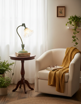 Flower table lamp on a round wooden table beside a cream armchair with mustard throw
