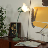 Flower table lamp lit on a teak sideboard beside a gold botanical framed print