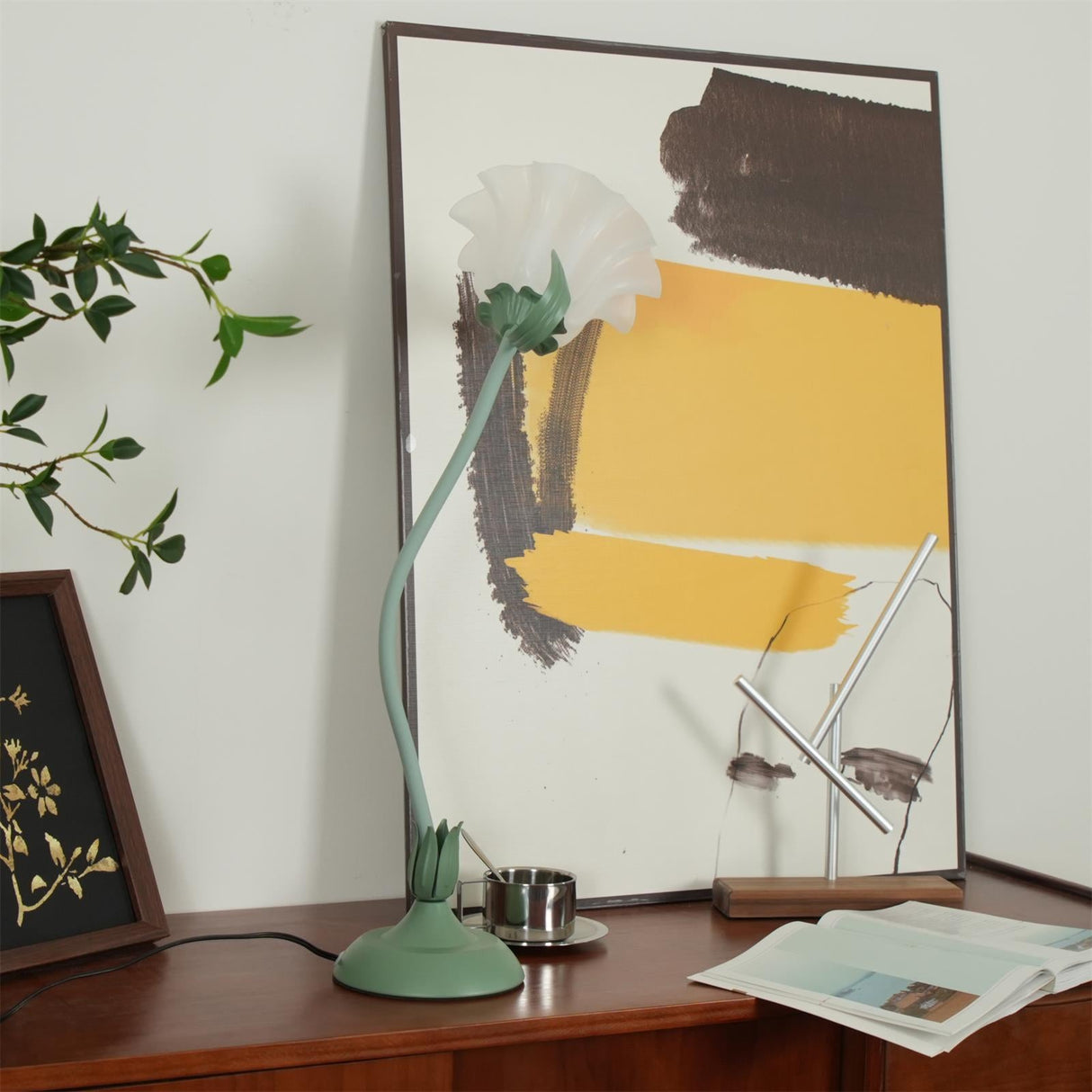 Flower table lamp with a wavy stem lit on a sideboard by an abstract print