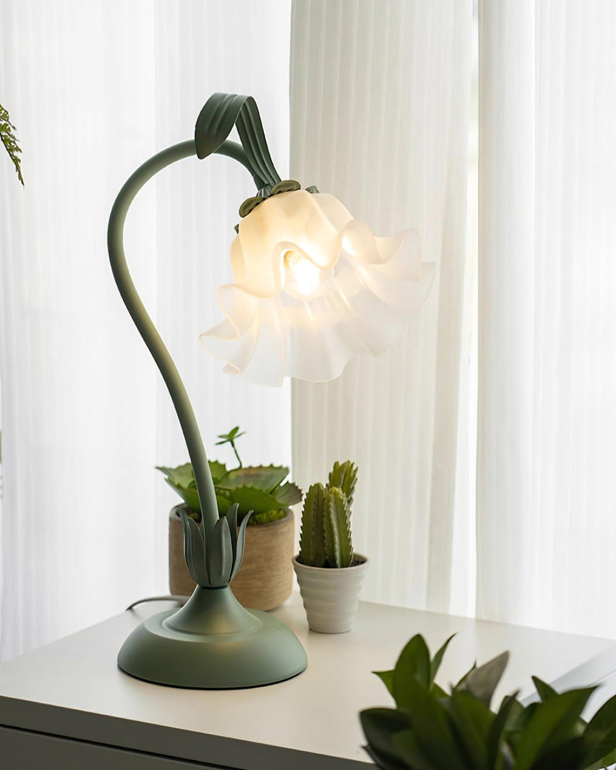Flower table lamp glowing on a white sill beside potted succulents and a cactus