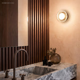 Gold ribbed wall light lit against a slatted timber bathroom wall