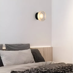 Ribbed acrylic wall light lit above a bed with grey linen