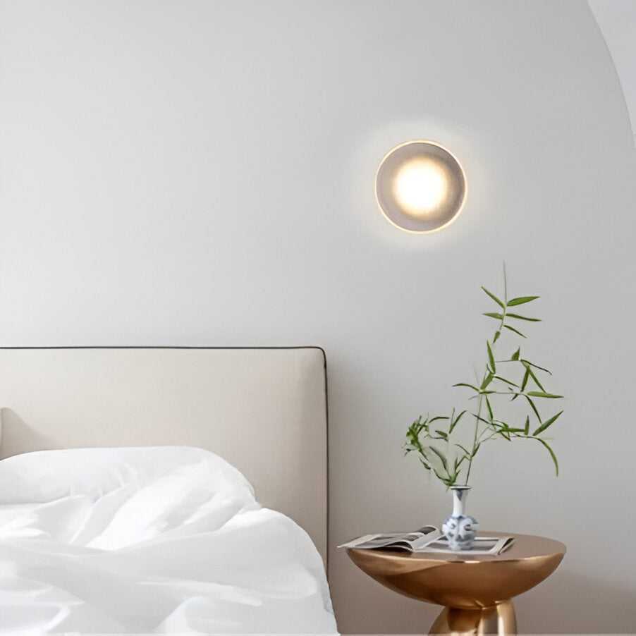 Ribbed disc wall light lit above a bedside table and small vase