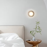 Ribbed disc wall light lit above a bedside table and small vase