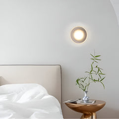 Ribbed disc wall light lit above a bedside table and small vase