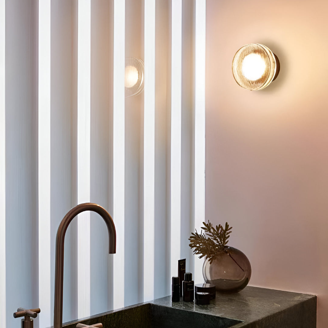 Gold ribbed wall light lit above a bedside table with a diffuser