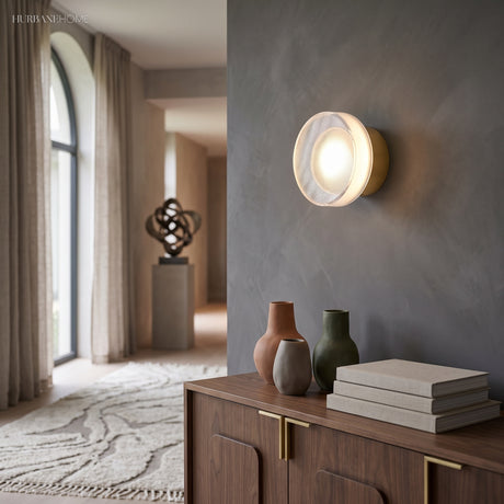 Gold ribbed disc wall light lit in a hallway above a sideboard