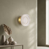 Gold ribbed acrylic wall light lit on an olive wall above vases