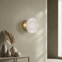 Gold ribbed acrylic wall light lit on an olive wall above vases