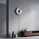 Silver disc wall light lit on a concrete wall above a sideboard
