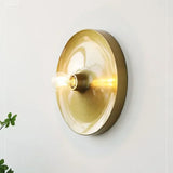Gold disc wall light lit warm with the bulb glowing at its centre
