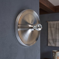 Brushed silver disc wall light with an exposed bulb on a grey wall