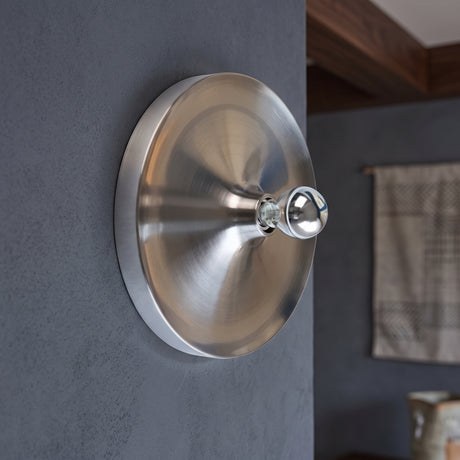 Brushed silver disc wall light with an exposed bulb on a grey wall