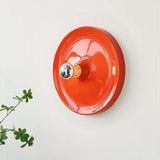 Orange disc wall light with a chrome bulb beside green leaves