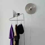 Silver ripple disc light above a clothes rail against a white wall