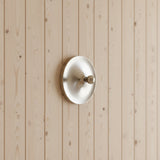 Silver disc light mounted on a pale timber clad wall