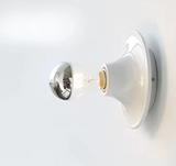 White disc wall light lit warm showing the exposed bulb