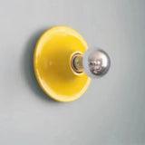 Yellow disc wall light with a mirrored bulb on a grey wall