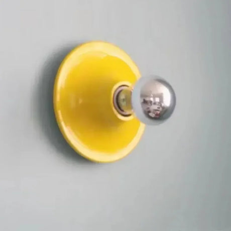 Yellow disc wall light with a mirrored bulb on a grey wall