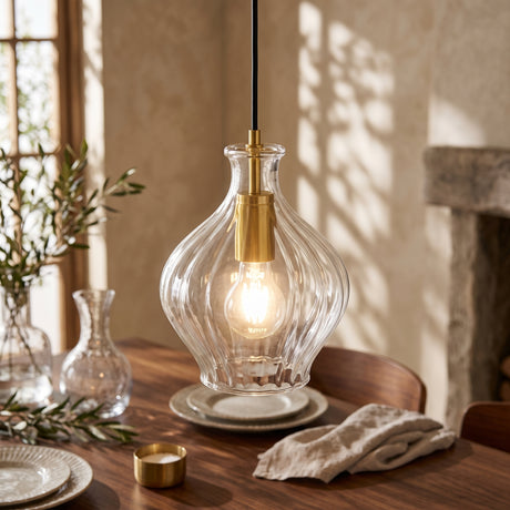 Clear fluted glass pendant with brass collar above a wooden dining table