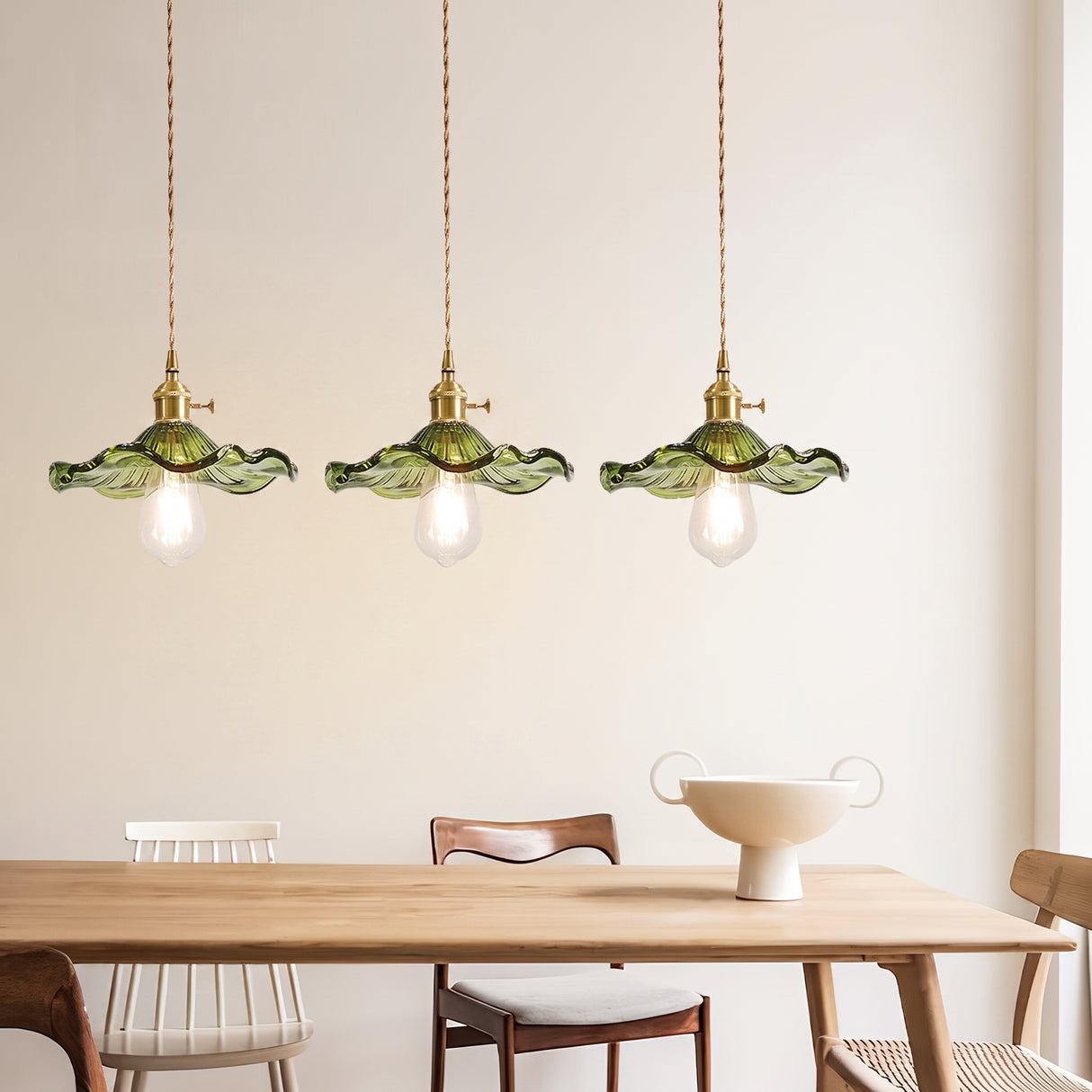 Three green scalloped glass pendants in a row above a light oak dining table
