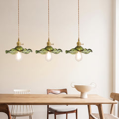Three green scalloped glass pendants in a row above a light oak dining table