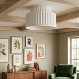 White two-tier fluted ceiling light close up under a wood-beamed ceiling above a green armchair