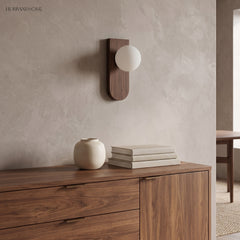 Frosted glass wall sconce above a walnut sideboard with vase and books