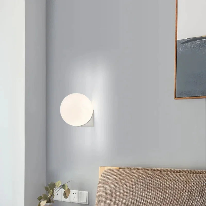 Silver finish globe wall lamp lit in a grey bedroom corner above a bed