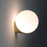 Single frosted glass globe on a gold wall bracket, lit against a grey wall