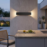 Black LED outdoor wall light on a concrete pillar above a patio dining table