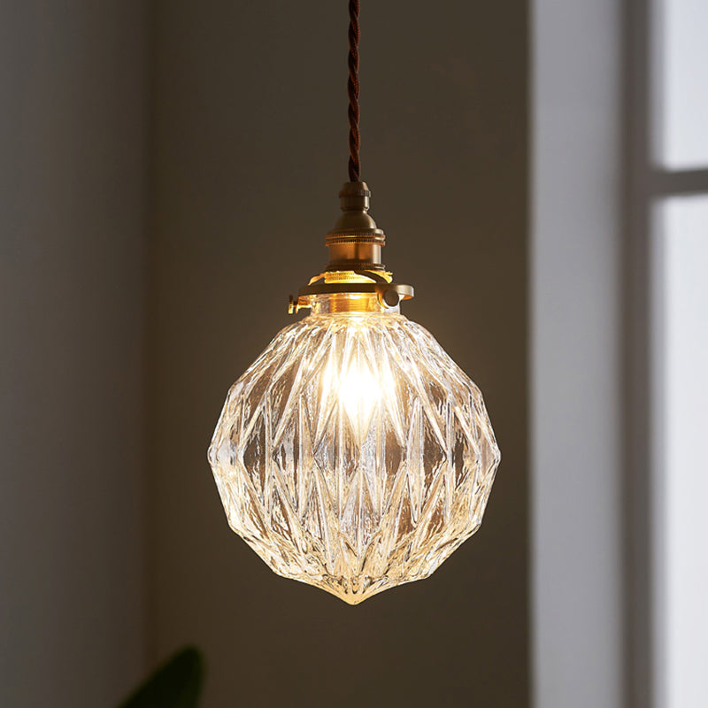 Faceted glass globe pendant lit close up against a pale wall