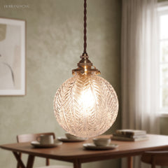 Leaf patterned glass globe lit above a dining table on green