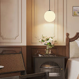 Opal globe pendant lighting a console table with flowers beside a bed