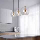 Three clear glass globe pendant lights in a row over a grey kitchen island