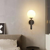 Black sconce with a white glass globe lit above a made bed