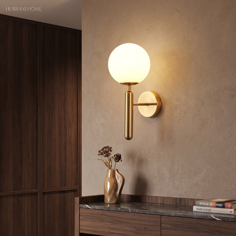 Gold sconce with a milk glass globe beside a dark wood wardrobe