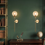 Pair of clear glass globe wall sconces on a green study wall by a bookshelf