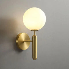 Gold wall sconce with a milk glass globe against a plain grey wall