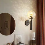 Black ripple glass sconce lit beside a round mirror and artwork