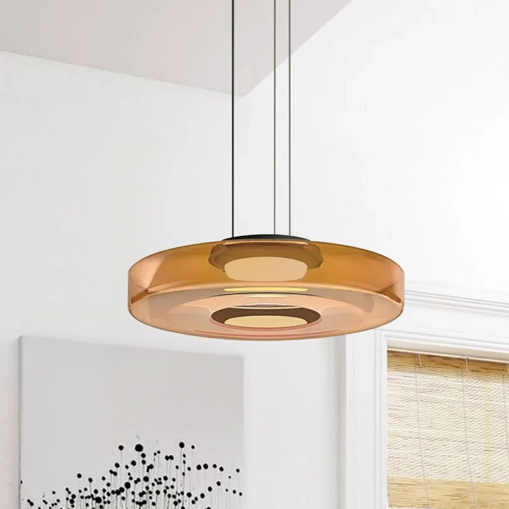 Single amber glass disc pendant light against a near-plain white wall with art